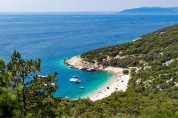 Pogled s visine na plažu Sveti Ivan ispod Lubenica na otoku Cresu, s tirkiznim morem, bijelim šljunkom, usidrenim brodovima i okruženjem guste mediteranske vegetacije.