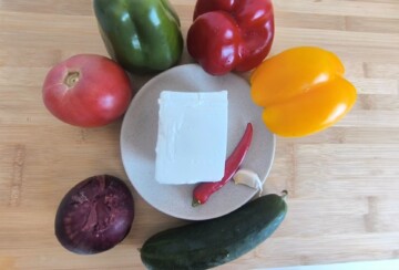 Sastojci za šopsku salatu raspoređeni oko tanjura s feta sirom: rajčice, paprika u tri boje, ljubičasti luk, krastavac, češnjak i ljuta papričica.