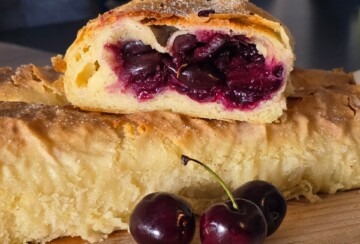 Domaća štrudla od trešanja s gotovim korama, prikazana s kriškom punom sočnih trešanja i nekoliko svježih plodova ispred.