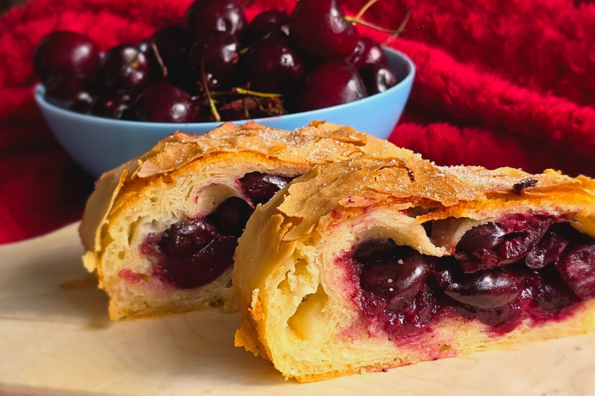 Štrudla od trešanja s gotovim korama, narezana i poslužena ispred zdjele punih svježih trešanja.