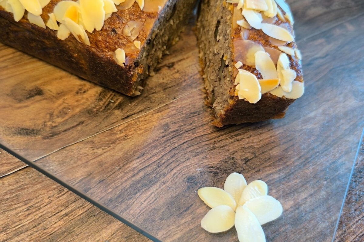 banana-bread-slatki-kruh Banana bread posut listićima badema, narezan na šnite, poslužen na drvenoj podlozi.