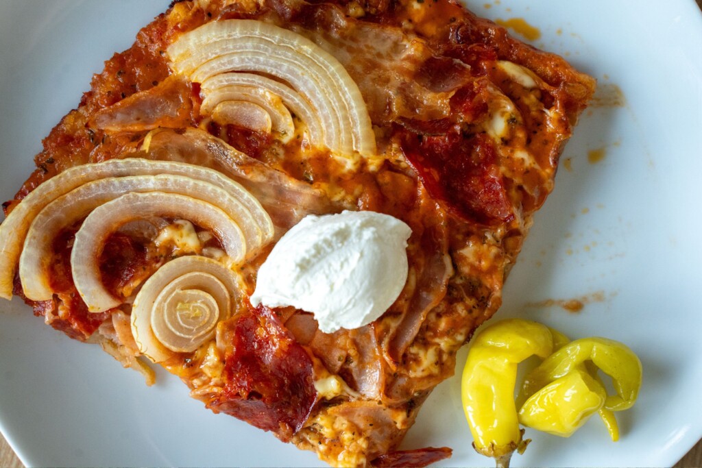Komad bezglutenske pizze poslužen s kiselim vrhnjem i papričicom