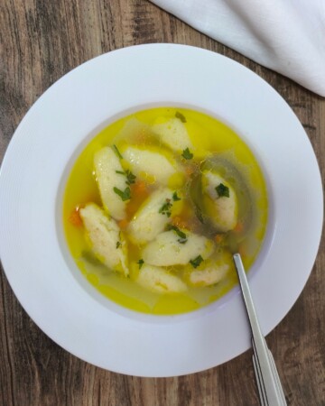 pileca-juha-s-noklicama-1 Bijeli tanjur pun pileće juhe s noklicama, mrkvom i svježim peršinom. Domaća pileća juha s noklicama – recept koji spaja jednostavne sastojke u savršenu juhu za svaku priliku, od ručka do svečane večere.