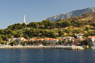 Pogled s mora na kuće u Podgori, spomenik Galebova krila i Biokovo u pozadini