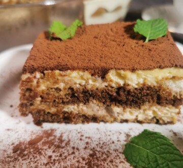Presjek tiramisua s vidljivim slojevima kreme i piškota, posut kakaom i dekoriran mentom.