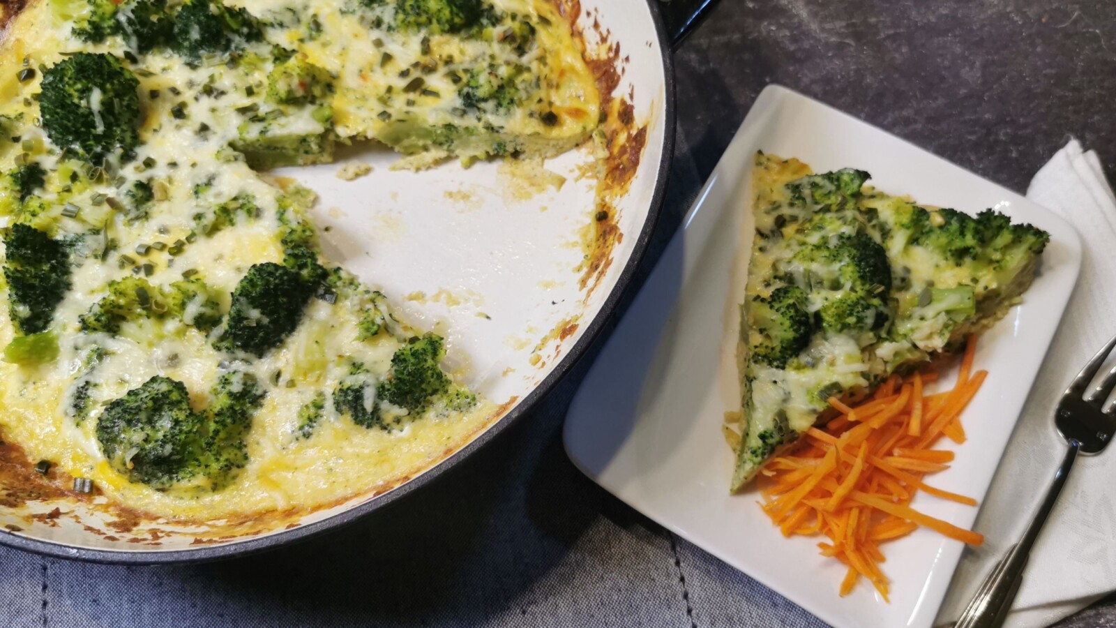 fritaja-od-brokule Zapečena fritaja od brokule u tavi, s izrezanim komadom na tanjuru uz ribanu mrkvu.