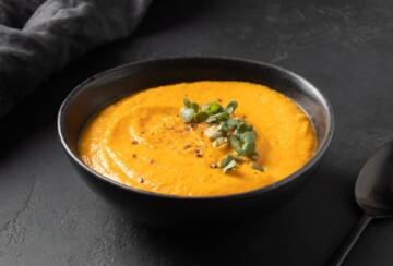 Krem juha od bundeve poslužena u crnoj zdjeli na tamnoj podlozi, ukrašena svježim začinskim biljem i bučinim sjemenkama. Gusti, narančasti sloj juhe odiše jesenskim bojama i teksturom savršeno pripremljene bundeve. Idealna fotografija za recept za juhu od butternut ili hokaido tikve, zdravo i sezonsko jelo bogato okusom i vitaminima.