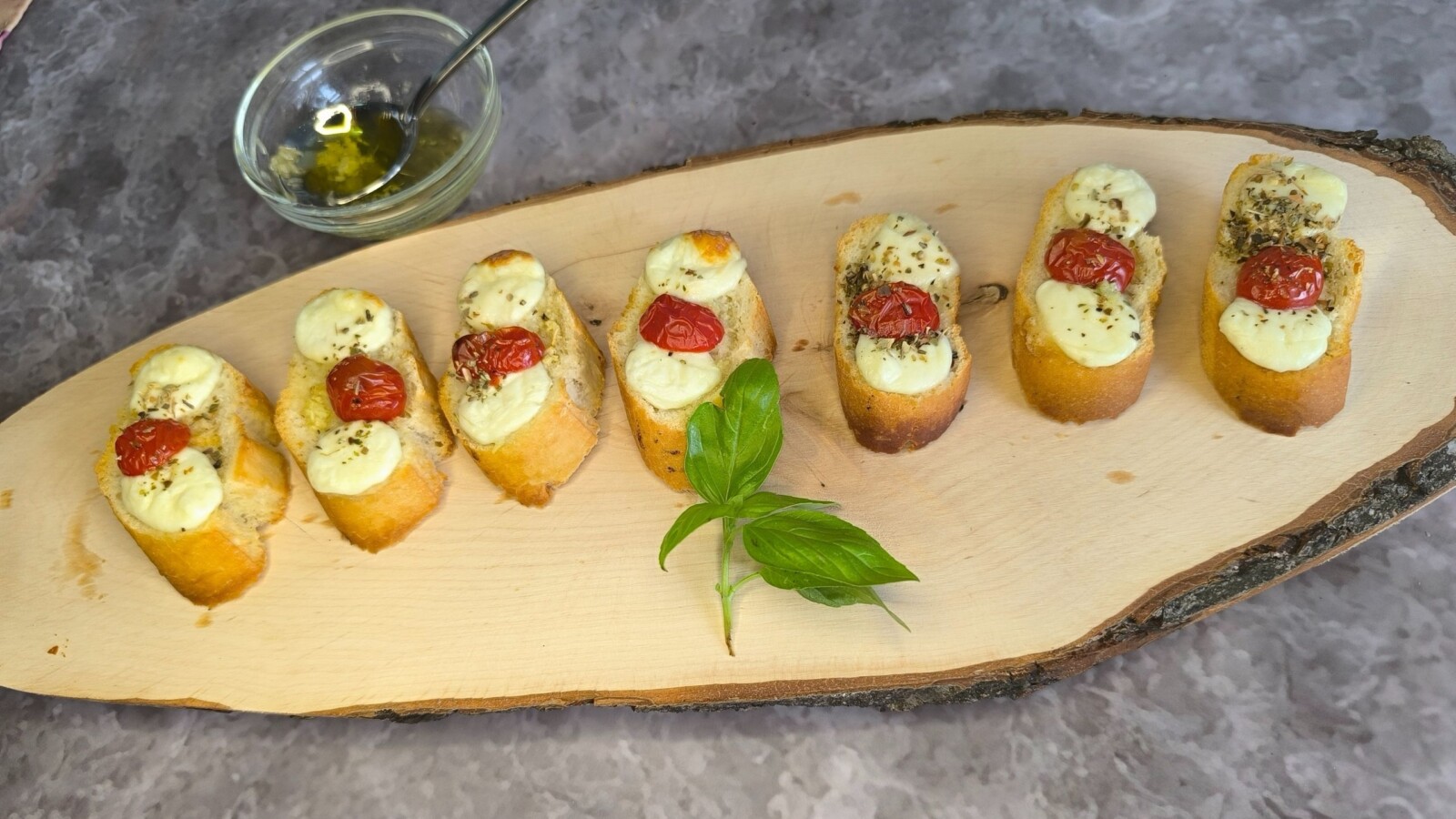 domace-bruschette Hrskave domaće bruschette iz pećnice s otopljenom mozzarellom, cherry rajčicama i bosiljkom, poslužene na drvenoj dasci uz aromatično maslinovo ulje.