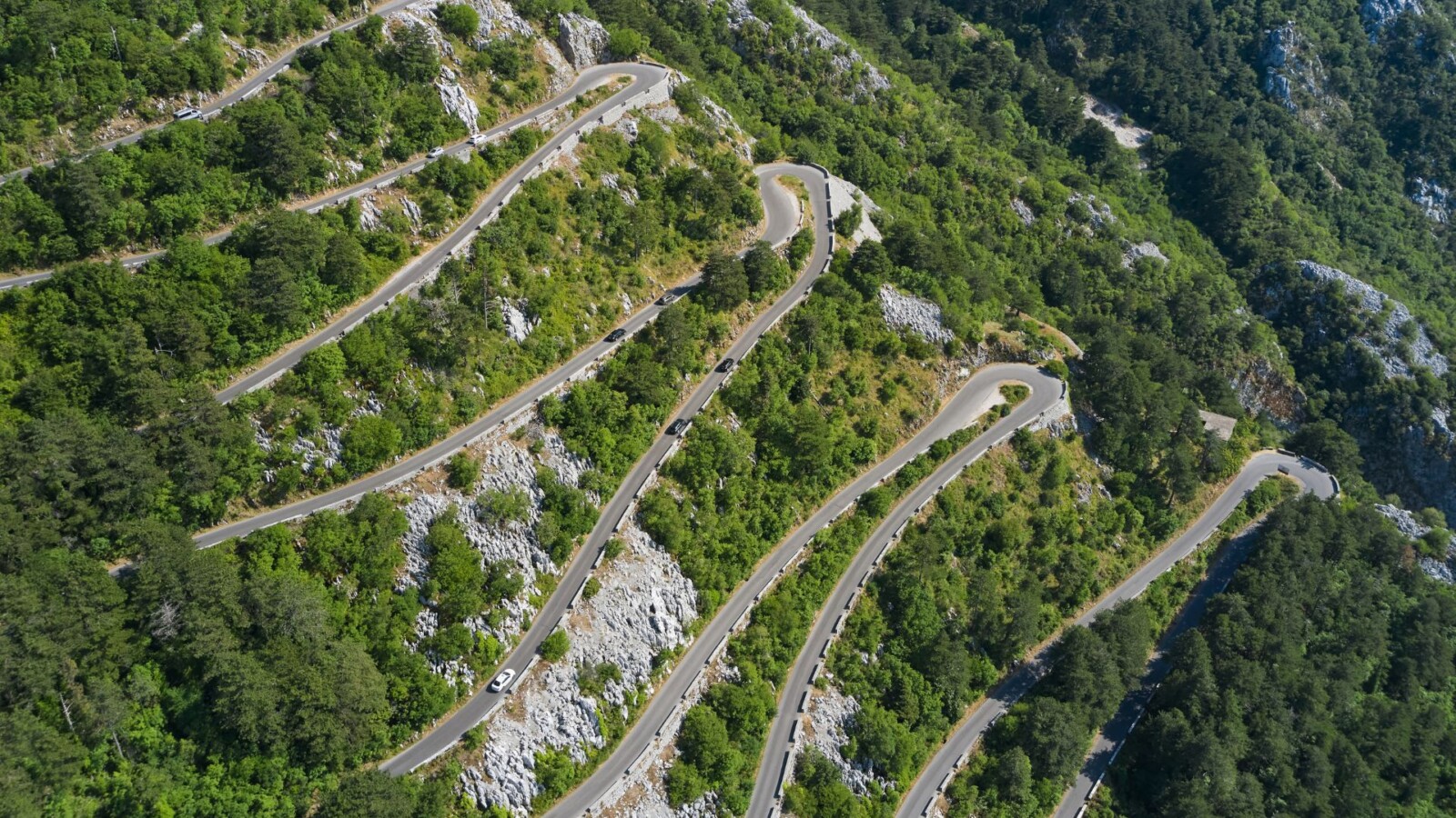 Zračni pogled na Kotorske serpentine na Starom kotorskom putu između Kotora i Lovćena, s nizom oštrih zavoja koji vijugaju kroz zelenilo planine.