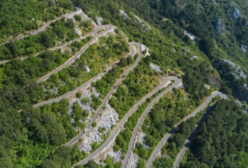 Zračni pogled na Kotorske serpentine na Starom kotorskom putu između Kotora i Lovćena, s nizom oštrih zavoja koji vijugaju kroz zelenilo planine.