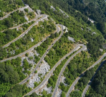 Zračni pogled na Kotorske serpentine na Starom kotorskom putu između Kotora i Lovćena, s nizom oštrih zavoja koji vijugaju kroz zelenilo planine.