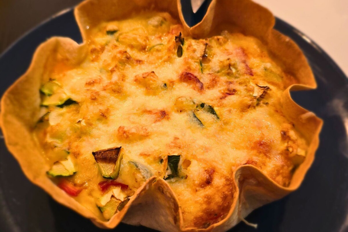 tortilja-iz-friteze-1 Hrskava tortilja s piletinom i povrćem iz friteze na vrući zrak poslužena na tamnom tanjuru; zlatno zapečen sir i sočno punjenje od tikvica, paprike i jaja čine savršen brzi ručak iz friteze.