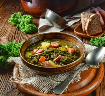 kelj-varivo-recept Tradicionalno hrvatsko kelj varivo s povrćem i kobasicom, prikazano u rustikalnom ambijentu uz kruh i svježe listove kelja.