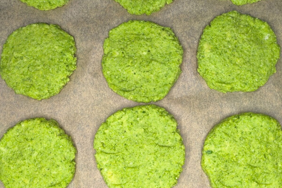 Oblikovane baze za pizzu od brokule poslagane na plehu spremne za pečenje.