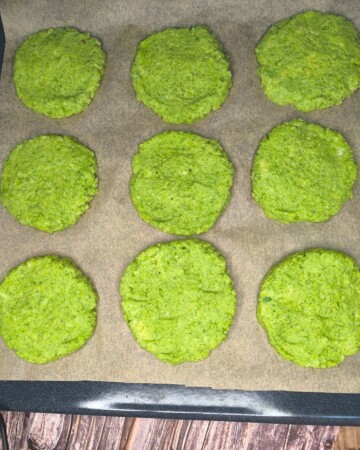 Oblikovane baze za pizzu od brokule poslagane na plehu spremne za pečenje.