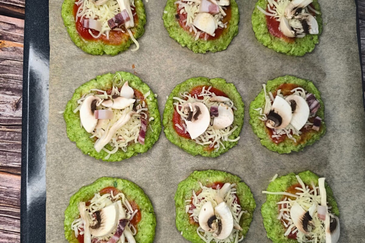 Mini pizza od brokule prije pečenja, obložena rajčicom, sirom i gljivama.
