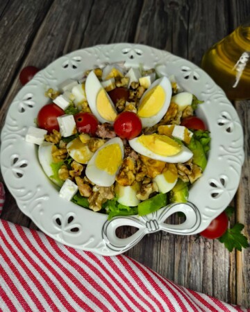 Salata s jajima, tunom i avokadom servirana na bijelom tanjuru, s cherry rajčicama i tostiranim orasima.