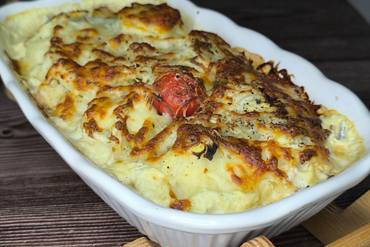 Zapečena cvjetača s rastopljenim sirom u bijeloj keramičkoj posudi, zlatno zapečena korica na vrhu