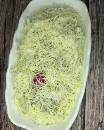 Cvjetača prekrivena naribanim sirom u posudi spremna za pećnicu.