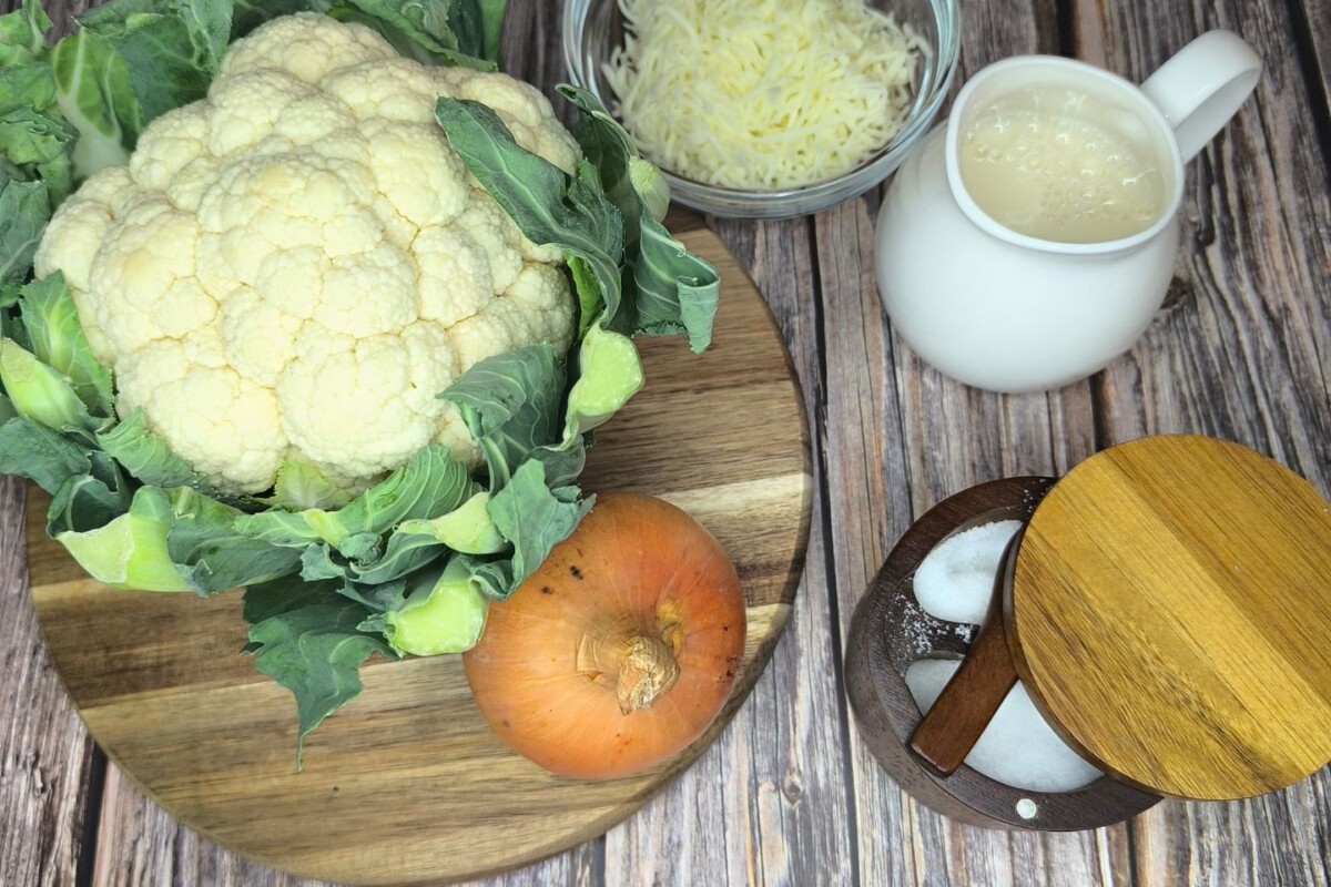 zapecena-cvjetaca-sastojci Svježa glavica cvjetače s naribanim sirom, jajima i začinima pripremljena za recept.