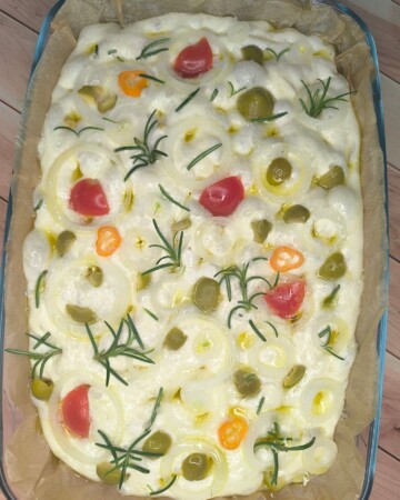focaccia-priprema-tijesta-2 Sirovo tijesto za focacciu prekriveno cherry rajčicama, maslinama i ružmarinom
